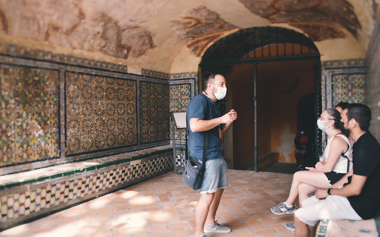 Guide explaining Alcázar's tiled walls to visitors on a tour.