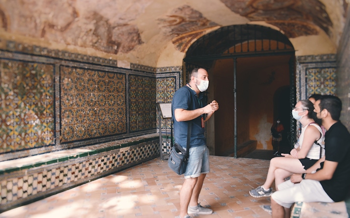 Guide explaining Alcázar's tiled walls to visitors on a tour.