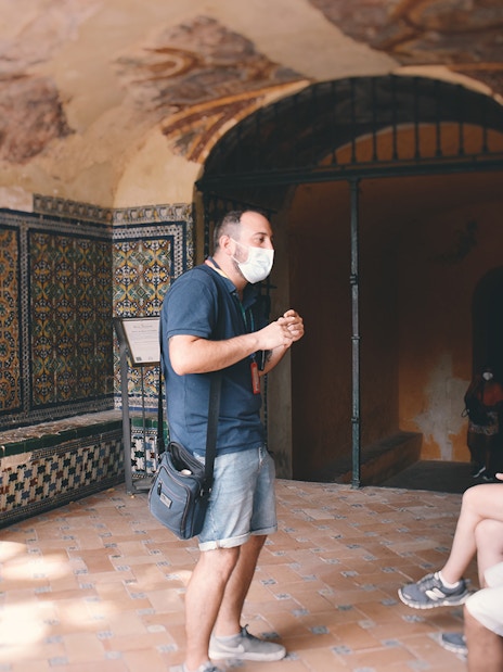 Guide explaining Alcázar's tiled walls to visitors on a tour.