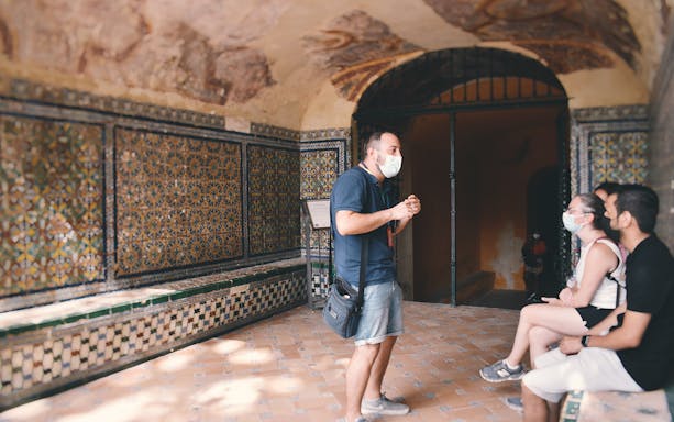 Guide explaining Alcázar's tiled walls to visitors on a tour.
