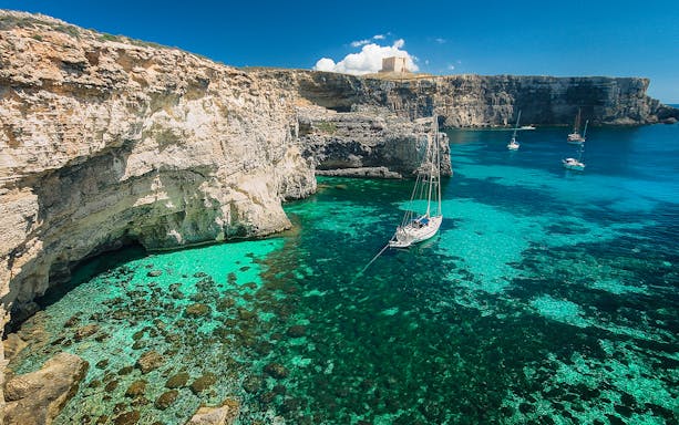 Boat cruising through Blue Lagoon's turquoise waters, surrounded by rocky cliffs, Malta.