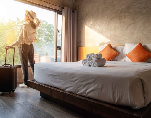 Traveler with suitcase in Istanbul hotel room, looking out window at sunrise.