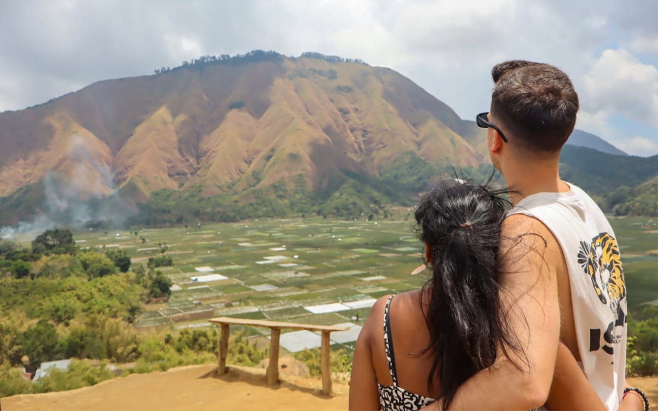 Couple enjoying the view at Bukit Selong Sunrise Viewpoint, Lombok with mountain backdrop.
