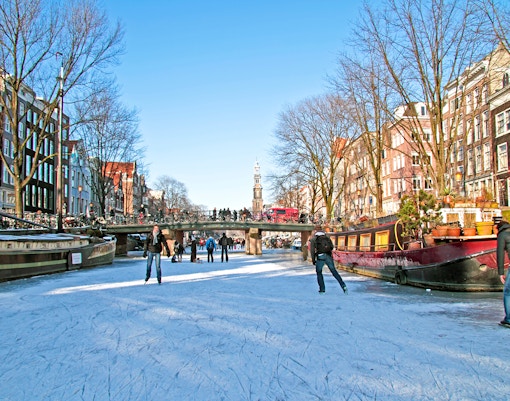 Ice skating on frozen Amsterdam canal with historic buildings in the background, Netherlands winter.