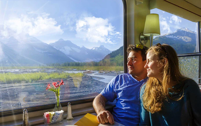 Couple enjoying scenic mountain views from Alaska Railroad train window.