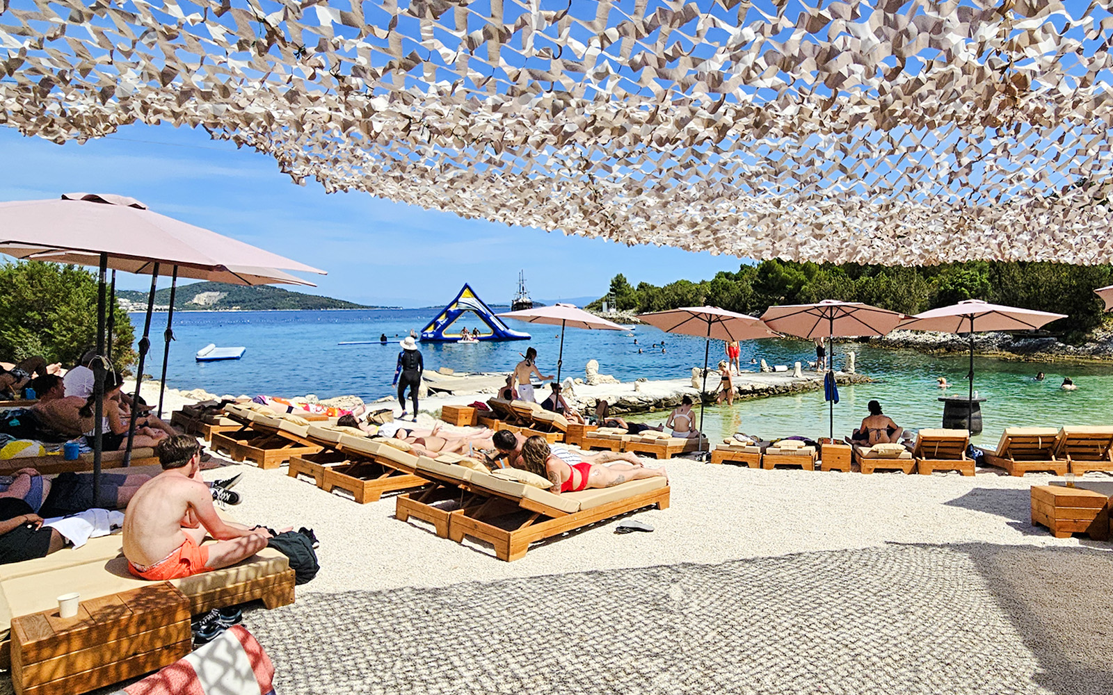 Sunbathers on loungers by the Blue Lagoon, Croatia, with inflatable water park in the background.