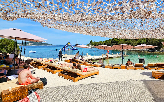 Sunbathers on loungers by the Blue Lagoon, Croatia, with inflatable water park in the background.