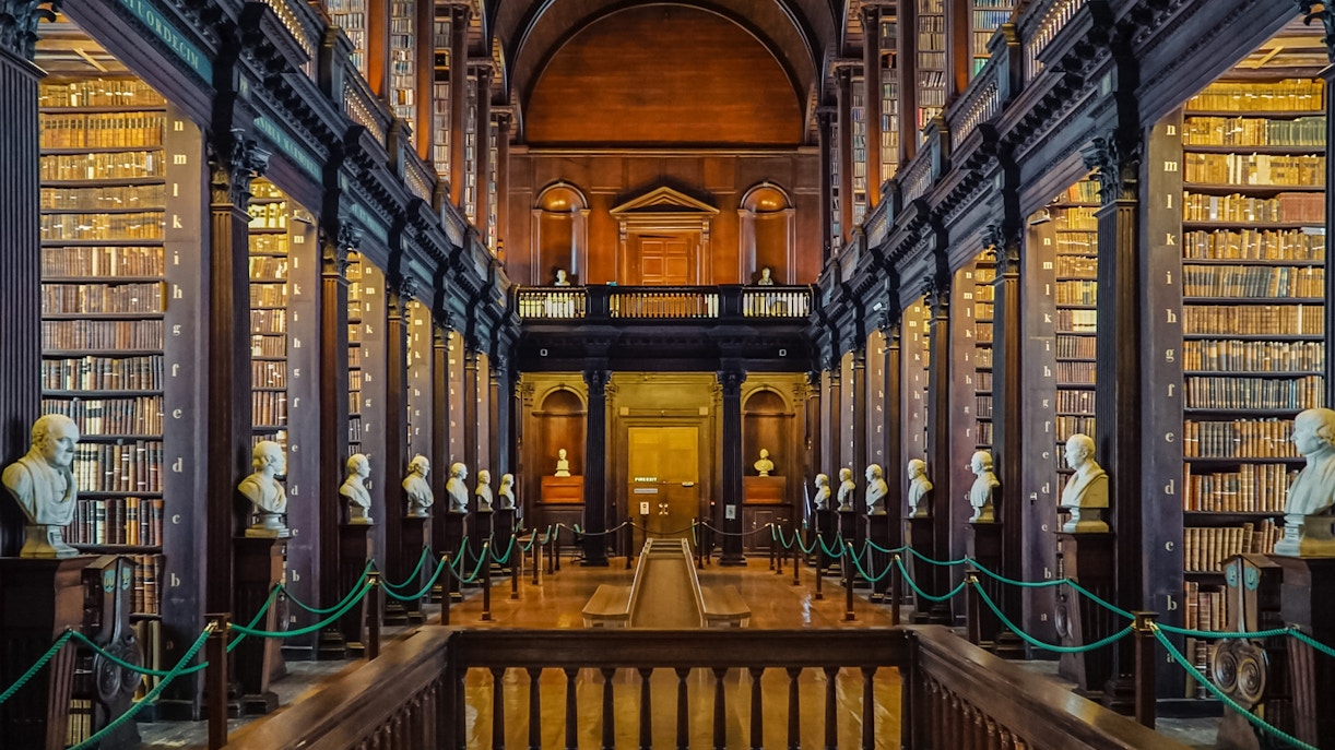 Library of Trinity College interior with visitors viewing the Book of Kells exhibit, Dublin, Ireland.