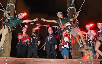 Participants on a night zipline adventure with glowing helmets, preparing for a ride.