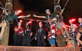 Participants on a night zipline adventure with glowing helmets, preparing for a ride.