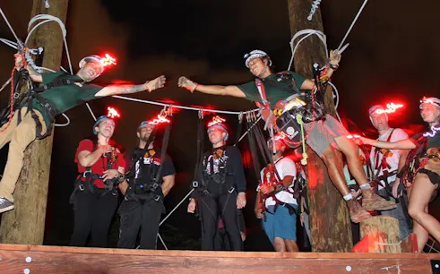 Participants on a night zipline adventure with glowing helmets, preparing for a ride.