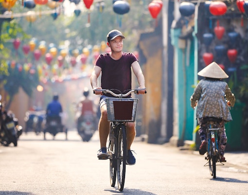 Tourist cycling through lantern-lined street in Hoi An, Vietnam.