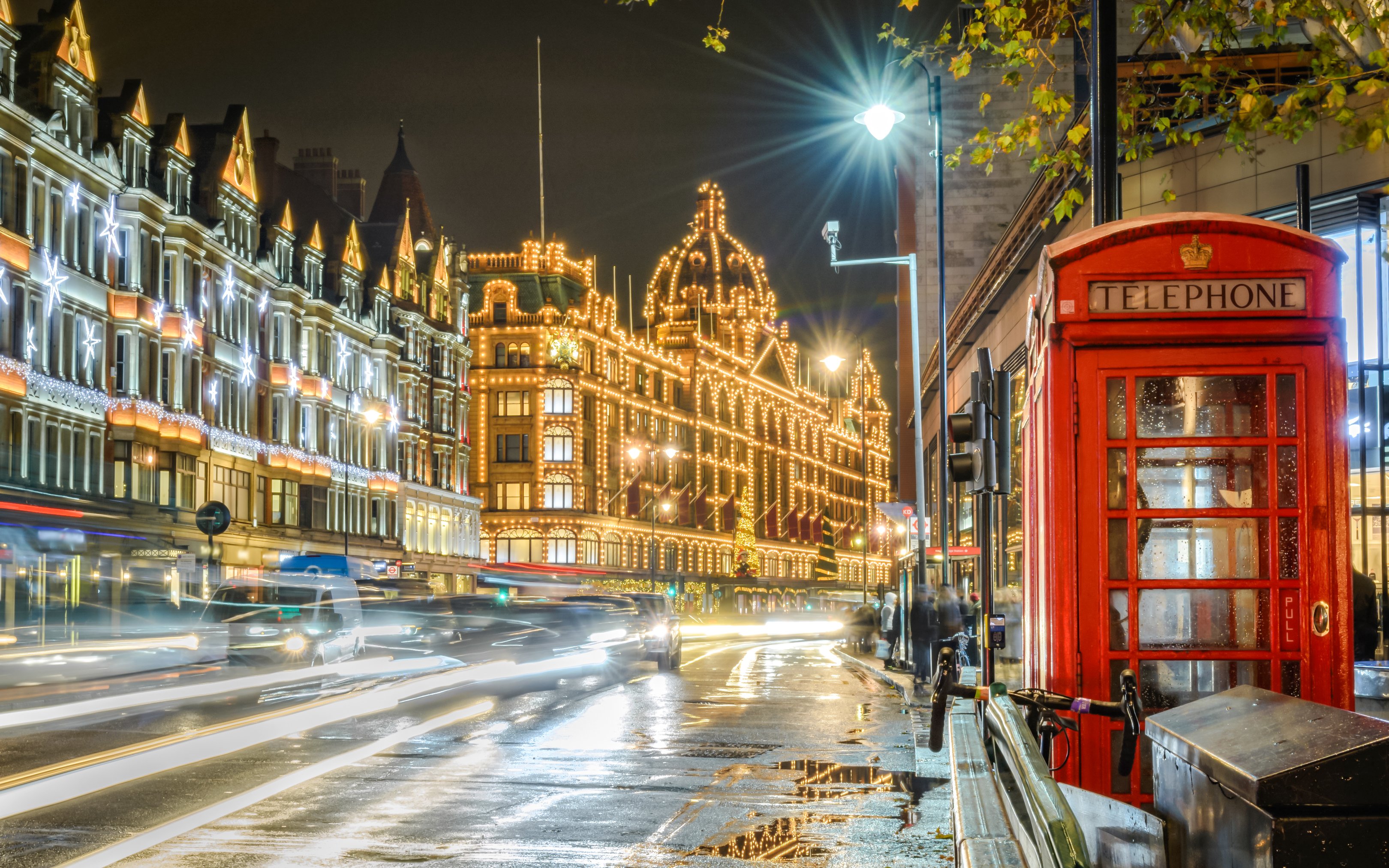 London street with Christmas lights, iconic red telephone booth, and Harrods in the background.