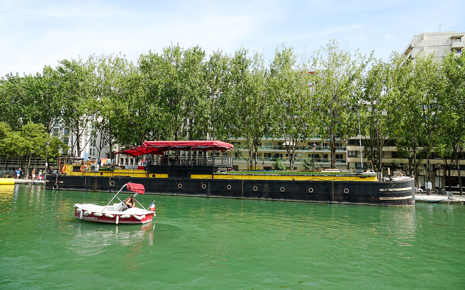 Boat on Bassin de la Villette, Paris with trees and buildings in the background.