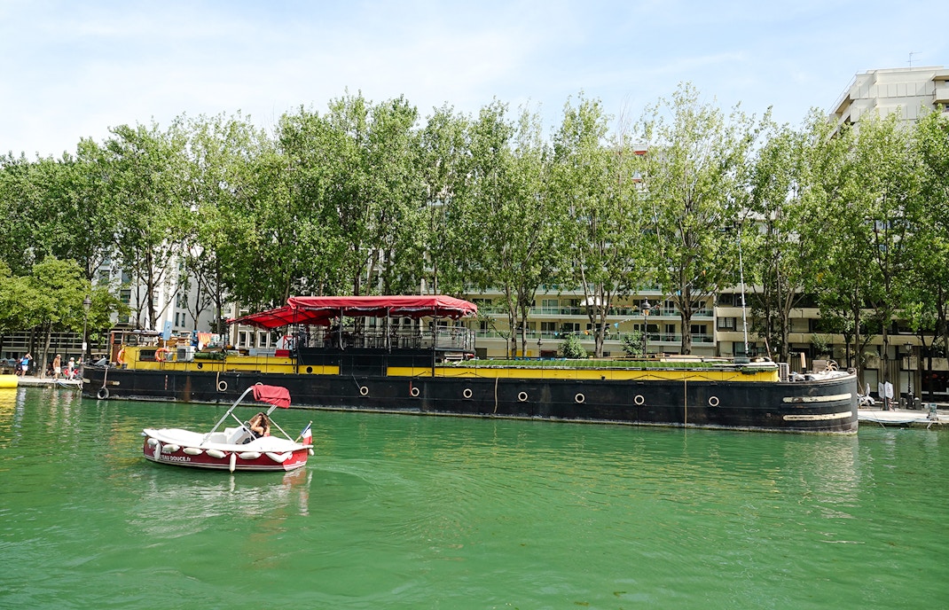 Boat on Bassin de la Villette, Paris with trees and buildings in the background.