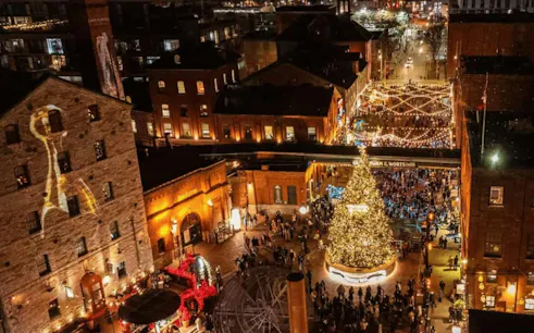 Distillery Winter Village lit up at night with festive lights and a large Christmas tree in Toronto.