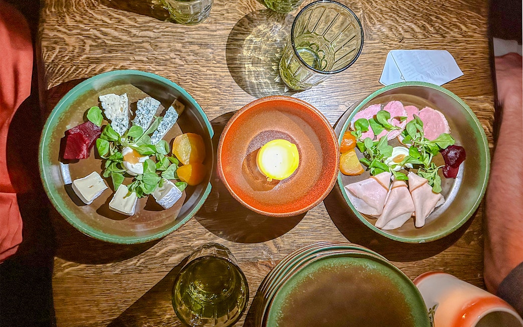 Medieval dinner table with assorted cheeses, meats, and a candle centerpiece.