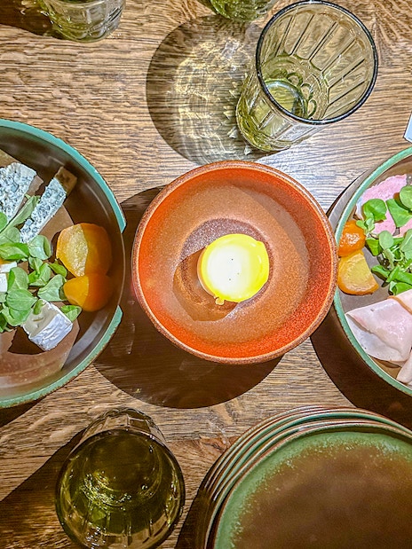 Medieval dinner table with assorted cheeses, meats, and a candle centerpiece.