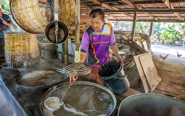 Man preparing traditional food at Damnoen Saduak Floating Market, Thailand.