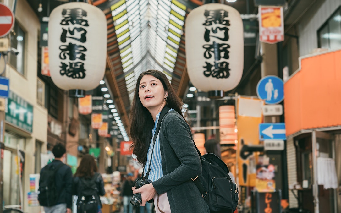 Tourist exploring Kuromon Ichiba Market in Osaka with camera.