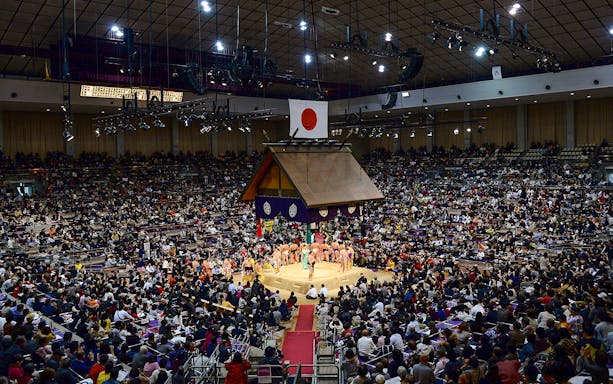 Sumo wrestlers in a crowded arena during the Fukuoka Sumo Tournament in Japan.