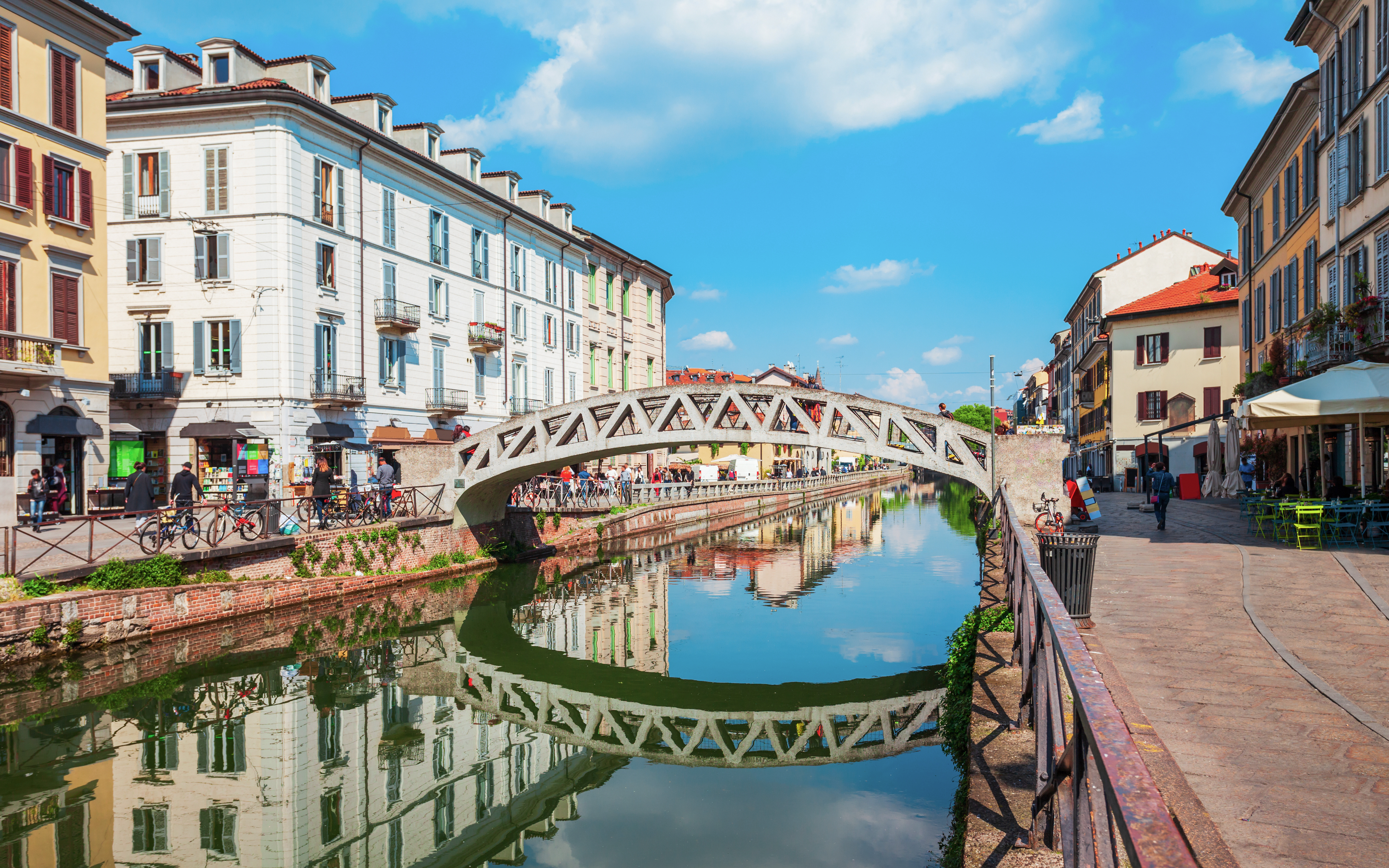 Pedestrian bridge over Navigli canals in Milan with reflections of historic buildings.