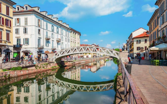 Pedestrian bridge over Navigli canals in Milan with reflections of historic buildings.