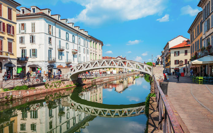 Pedestrian bridge over Navigli canals in Milan with reflections of historic buildings.