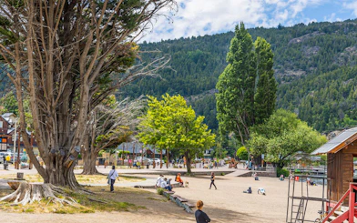 Public square with people and alpine-style buildings in San Martín de los Andes.