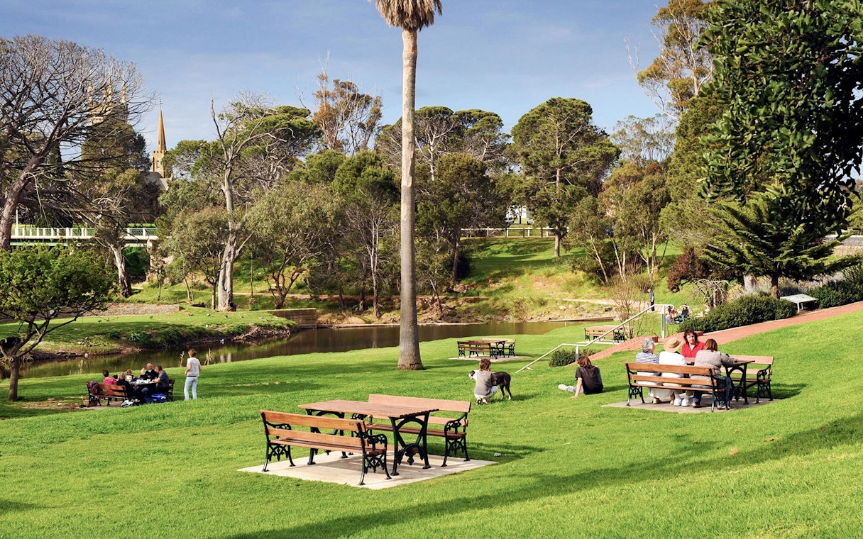 People enjoying a picnic in a park at Victor Harbor, surrounded by trees and a small river.