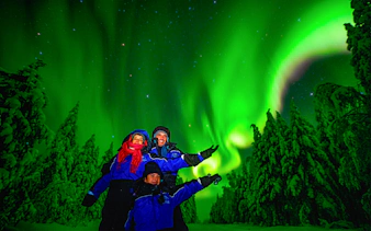 Family enjoying Northern Lights over snowy forest in Rovaniemi, Finland.