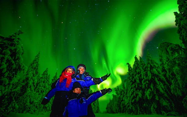 Family enjoying Northern Lights over snowy forest in Rovaniemi, Finland.
