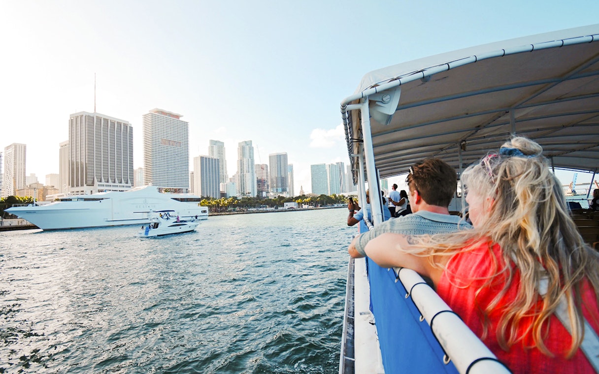 Guests enjoying a cruise with a view of Miami skyline and boats on the water.