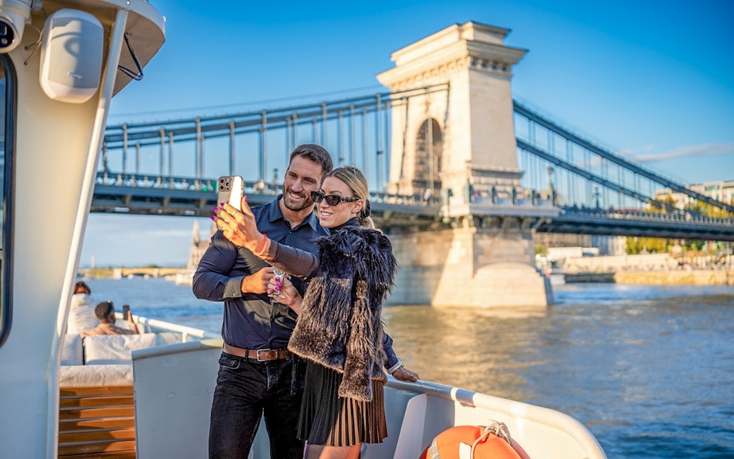 Guests taking a selfie on a cruise with Budapest's Chain Bridge in the background.