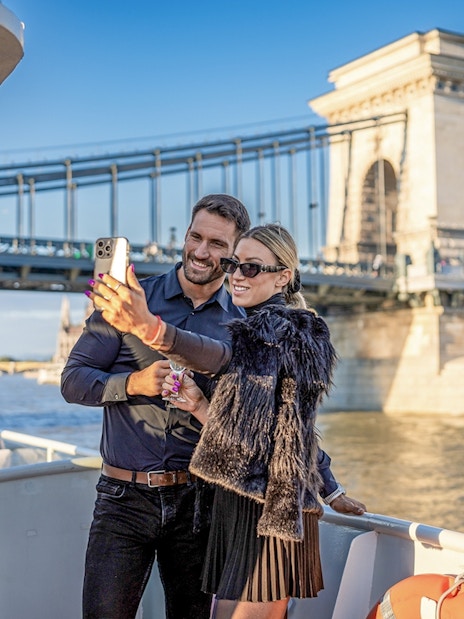 Guests taking a selfie on a cruise with Budapest's Chain Bridge in the background.