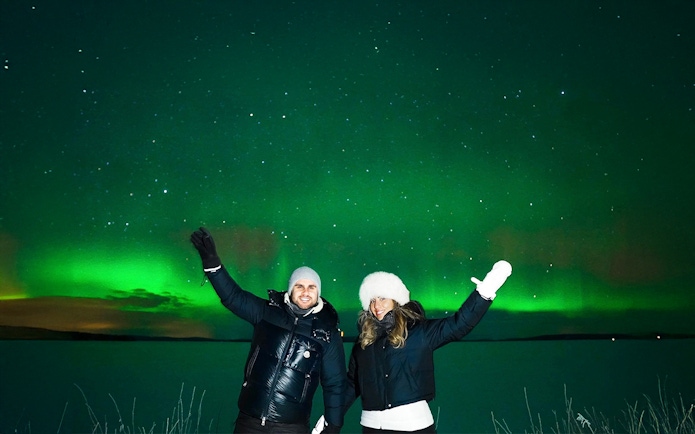 Northern Lights over snowy landscape with two people on Tromso Northern Lights Chase Tour.