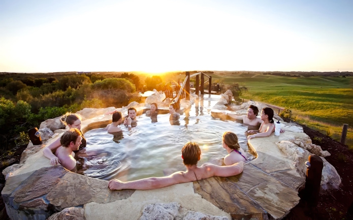 People relaxing in a hot spring pool at Peninsula Hot Springs during sunset.