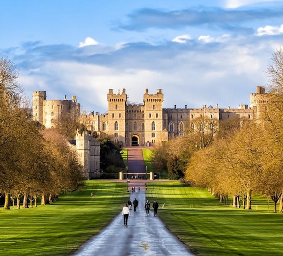 Windsor Castle with visitors walking along the Long Walk path.