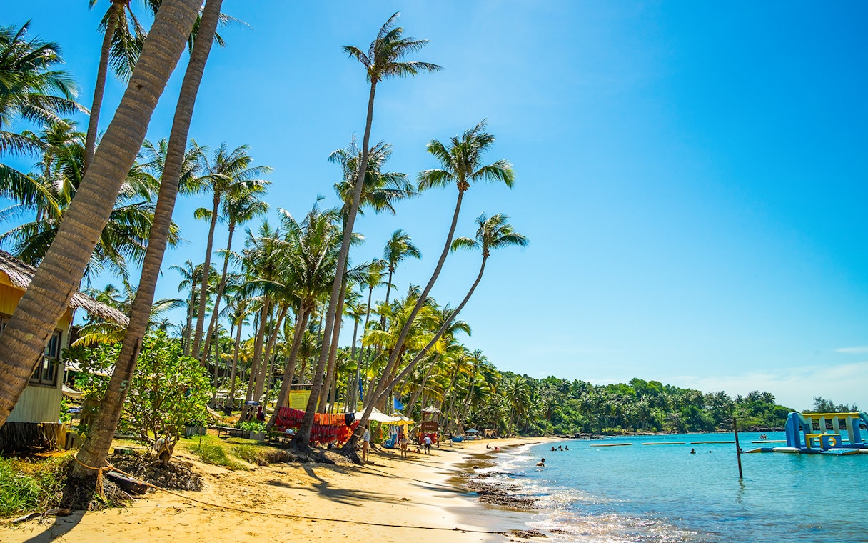 Hon Thom beach in Phu Quoc with palm trees and people swimming in clear blue water.