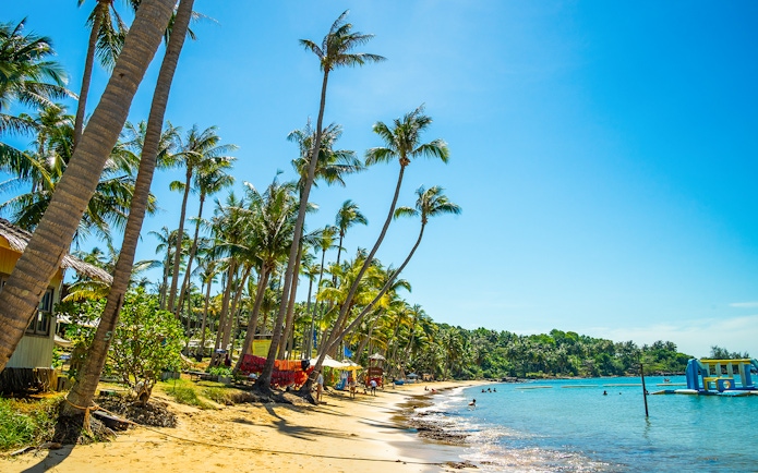 Hon Thom beach in Phu Quoc with palm trees and people swimming in clear blue water.