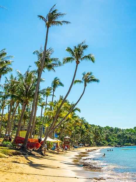 Hon Thom beach in Phu Quoc with palm trees and people swimming in clear blue water.