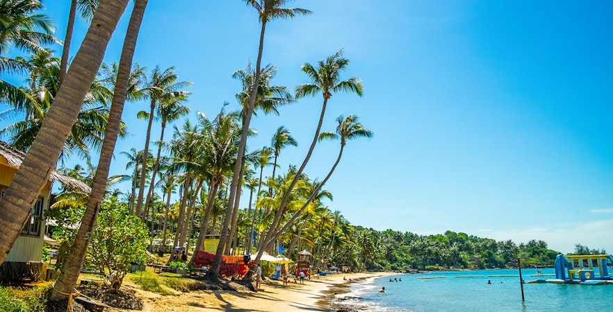 Hon Thom beach in Phu Quoc with palm trees and people swimming in clear blue water.