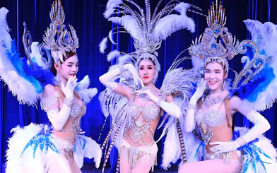 Performers in elaborate costumes at Miracle Cabaret Show, featuring feathered headdresses and sparkling outfits.
