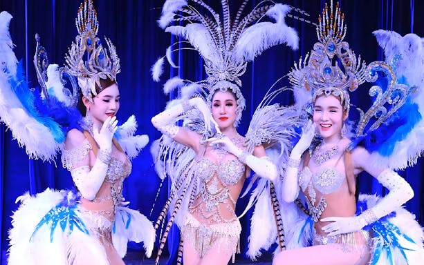 Performers in elaborate costumes at Miracle Cabaret Show, featuring feathered headdresses and sparkling outfits.