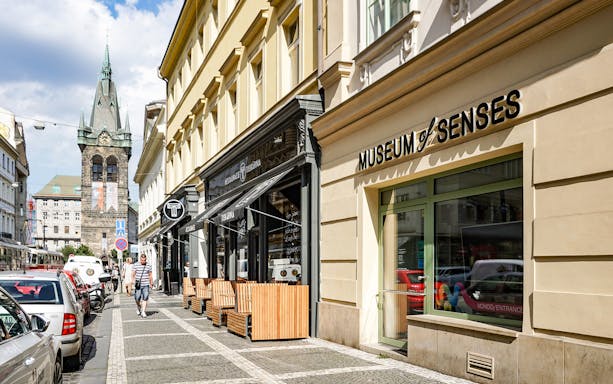 Entrance to the Museum of Senses on a busy street with a historic tower in the background.