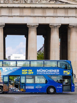 Blue double-decker bus for Munich hop-on-hop-off tour in front of historic columns.