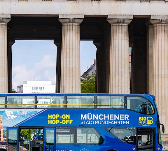 Blue double-decker bus for Munich hop-on-hop-off tour in front of historic columns.