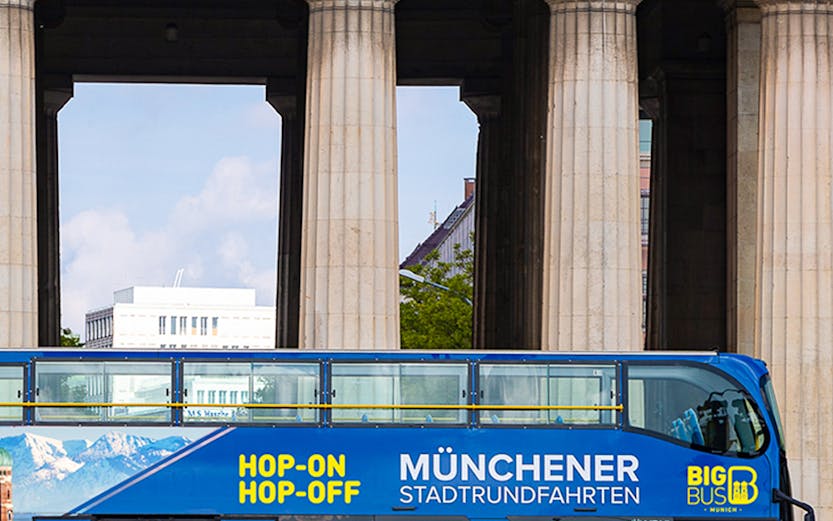 Blue double-decker bus for Munich hop-on-hop-off tour in front of historic columns.