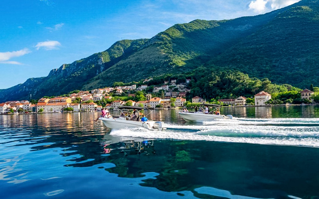 Speedboats on Bay of Kotor with mountain and village backdrop during Blue Cave tour.