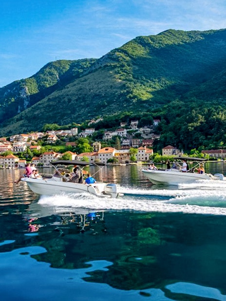 Speedboats on Bay of Kotor with mountain and village backdrop during Blue Cave tour.